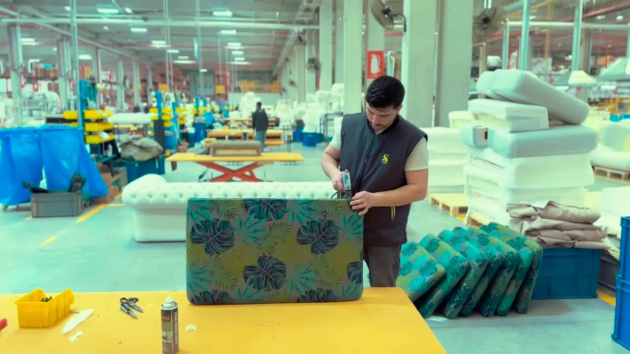 A craftsman upholstering a tropical-print cushion on a bright factory floor